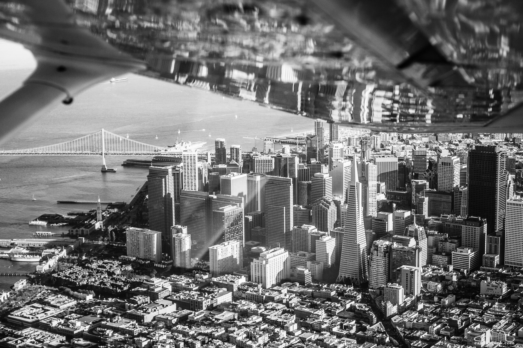 Downtown San Francisco reflected in the wing of a small Cessna plane. As a bonus, an aircraft carrier is anchored just near the Bay Bridge during Fleet Week.