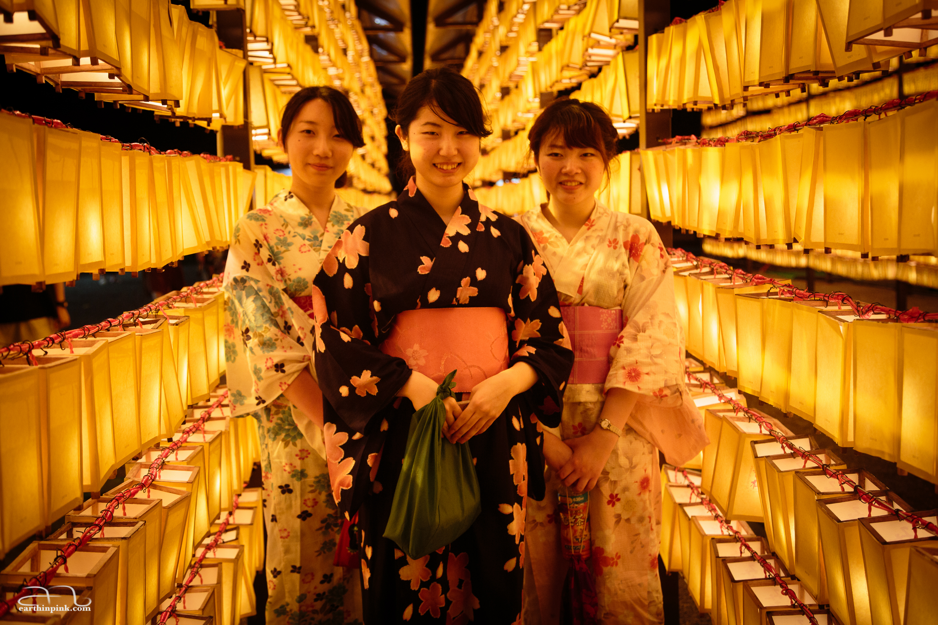 Girls wearing traditional summer yukatas stroll among the lanterns in front of Yasukuni shrine.