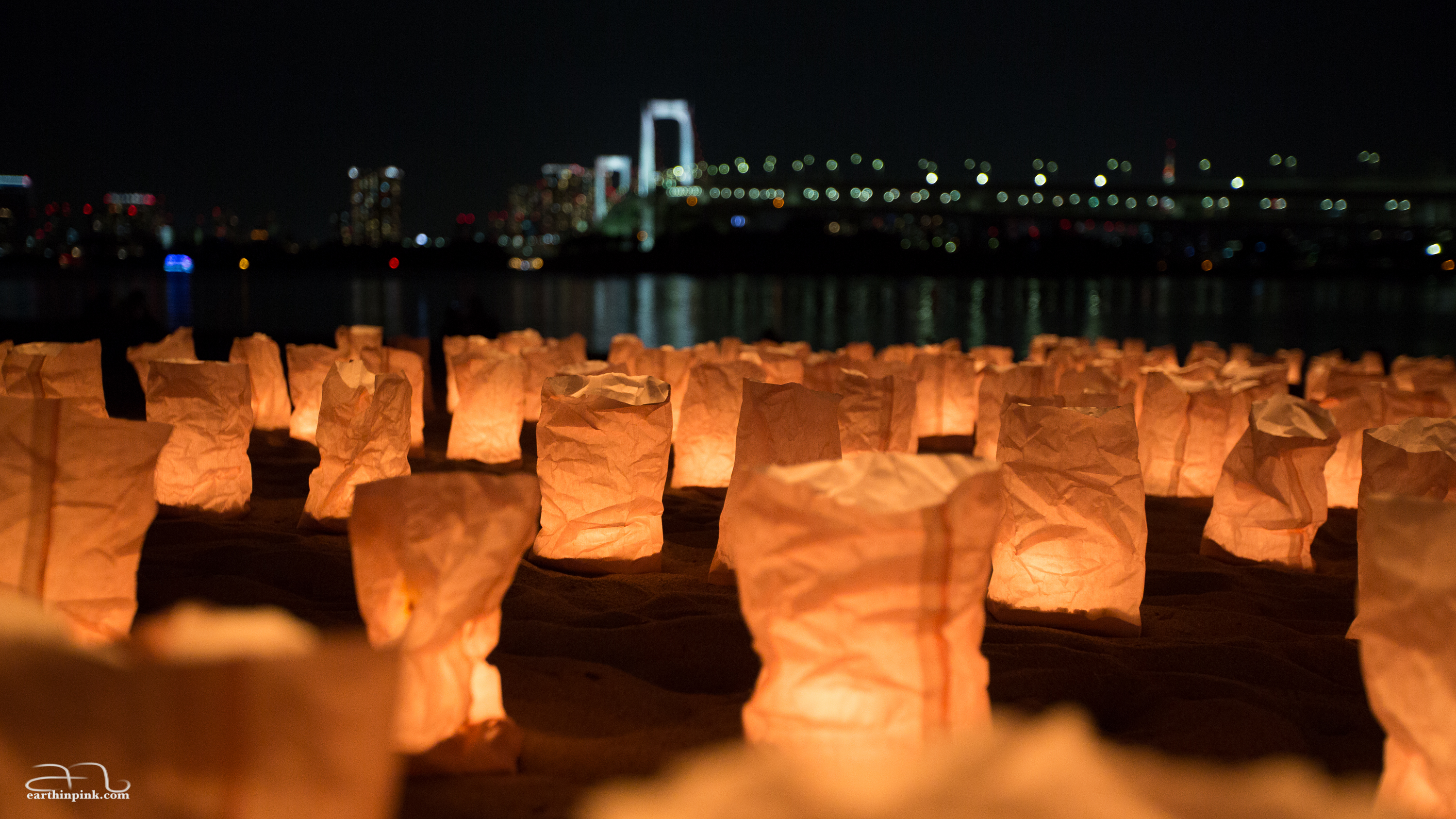 A focus on the paper bags used as lampions on the beach, with Odaiba's rainbow bridge in the distance.