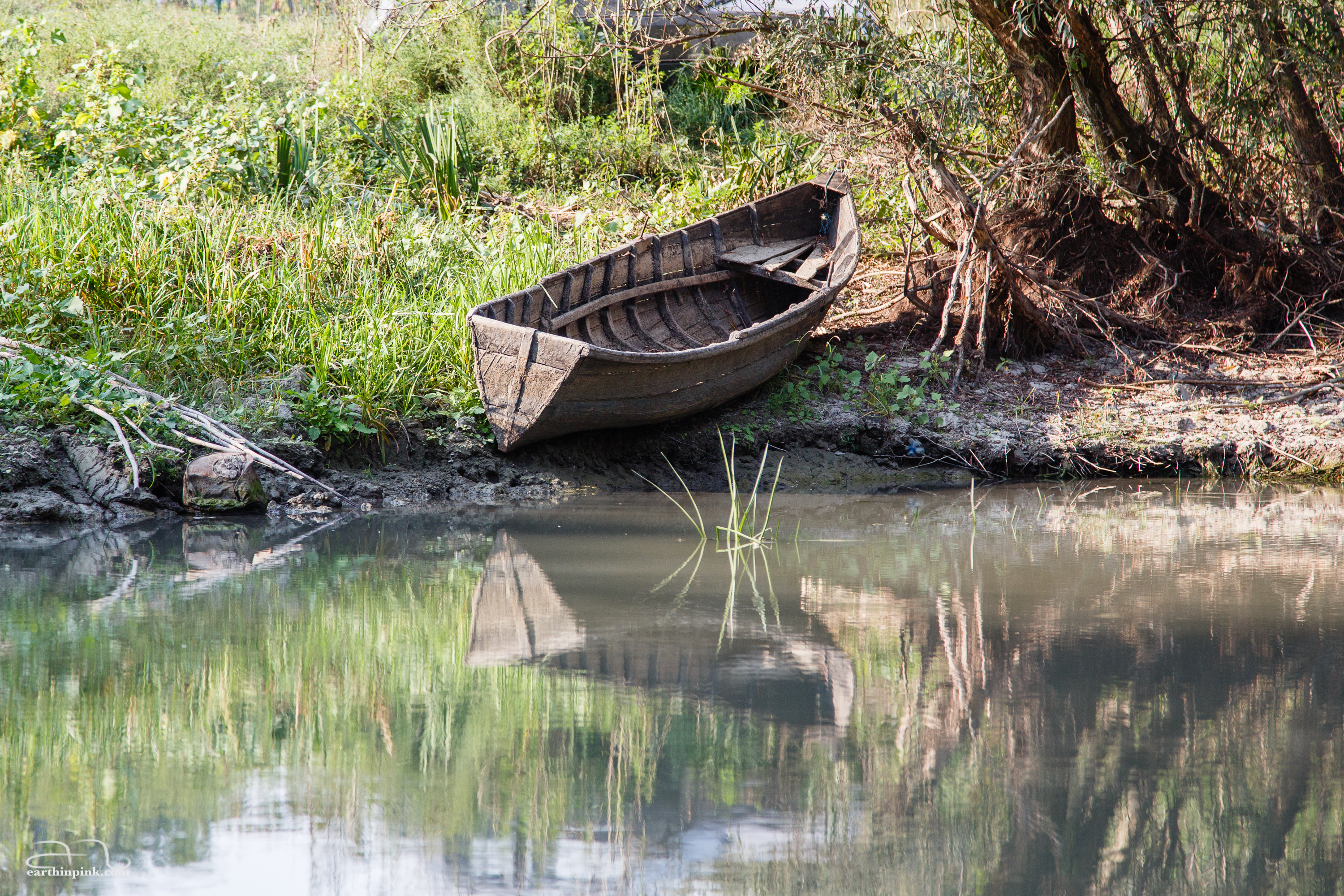 A small wooden boat by the side of a canal is reflected on the surface of the water